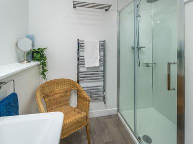 A bathroom with a wicker chair glass shower door towel radiator and a small mirror at The Indigo House in Berwick-Upon-Tweed