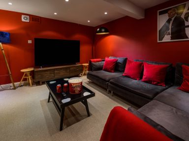 A living room with a large television on a wooden stand and a black coffee table with popcorn and soda cans at The Indigo House in Berwick-Upon-Tweed