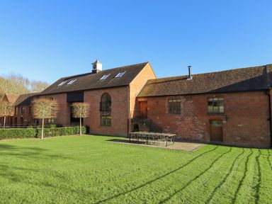 A large brick building with multiple windows and a clock tower and outdoor seating on grass at The Millhouse in Ledbury near Welland