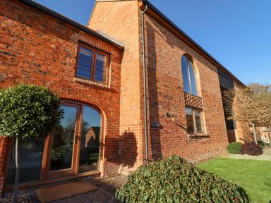 The exterior of a brick house with arched glass doors and windows and plants in front at The Millhouse in Ledbury near Welland