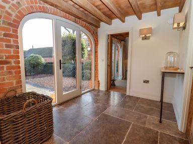 An entryway with stone tile flooring a wicker basket a small table with a glass cloche wall lights and arched glass doors at The Millhouse in Ledbury near Welland