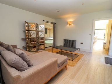 A living room with a sectional sofa a coffee table a decorative room divider and a view into another room at The Millhouse in Ledbury near Welland