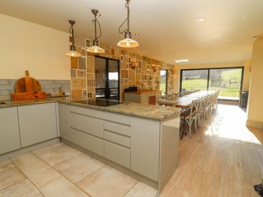 A kitchen with an island countertop and a long dining table with chairs near large windows at The Millhouse in Ledbury near Welland