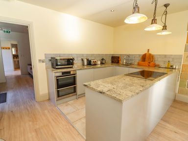 A kitchen with a countertop, stove, microwave, toaster, kettle, and cutting boards at The Millhouse in Ledbury near Welland