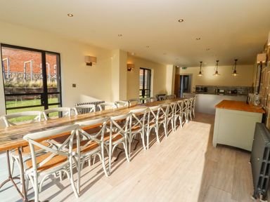 A dining room with a long wooden table and white chairs next to glass doors at The Millhouse in Ledbury near Welland
