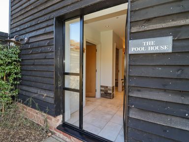 An open glass door showing a hallway with tiled floor and wooden doors at The Pool House