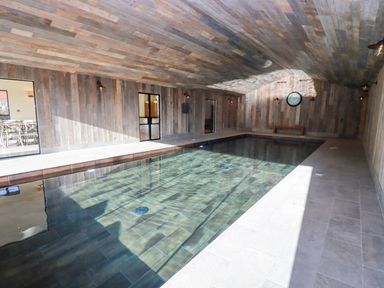 An indoor swimming pool with tiled floor and wooden paneled walls and ceiling at The Millhouse in Ledbury near Welland
