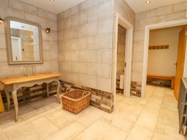 A tiled hallway with a wooden table mirror and wicker basket at The Millhouse in Ledbury near Welland