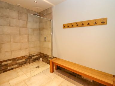 A tiled shower area with a glass screen a wooden bench and a coat rack with hooks at The Millhouse in Ledbury near Welland