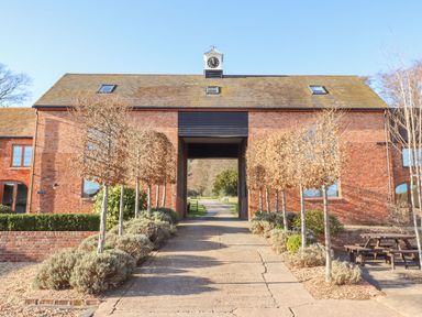 A paved driveway lined with pruned trees leading to a brick building with a clock tower at The Millhouse in Ledbury near Welland