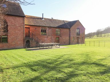 A brick building with outdoor seating on a patio and a large grass field at The Millhouse in Ledbury near Welland