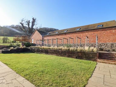 A garden with grass a stone path and a brick building with skylights at The Millhouse in Ledbury near Welland