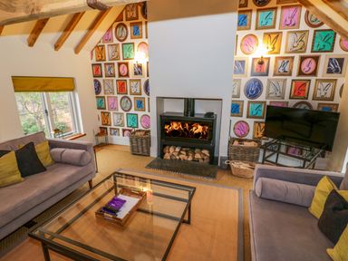 A living room with two sofas a glass coffee table a wood burning stove and framed rabbit artwork on the walls at The Millhouse in Ledbury near Welland