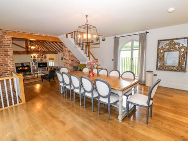 A dining room with a long wooden table surrounded by chairs next to a large window and an ornate mirror at The Millhouse in Ledbury near Welland