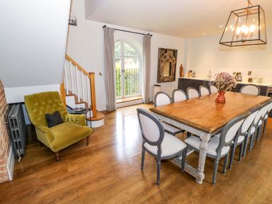 A dining room with a large wooden table surrounded by chairs and a green armchair near stairs at The Millhouse in Ledbury near Welland