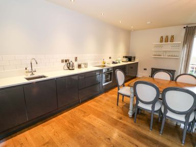 A kitchen with dark lower cabinets a wooden dining table with six chairs and shelves with jars and glasses at The Millhouse in Ledbury near Welland
