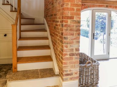 A wooden staircase with brick wall and white door leading outside with a wicker basket at The Millhouse in Ledbury near Welland