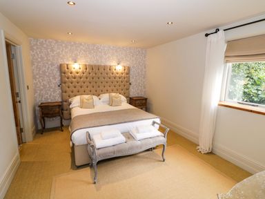 A bedroom with a bed, upholstered headboard, bedside tables, and a window at The Millhouse in Ledbury near Welland