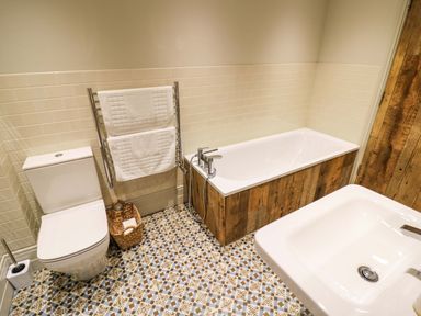 A bathroom with a bathtub, toilet, sink, towel rack, and patterned floor tiles at The Millhouse Ledbury near Welland