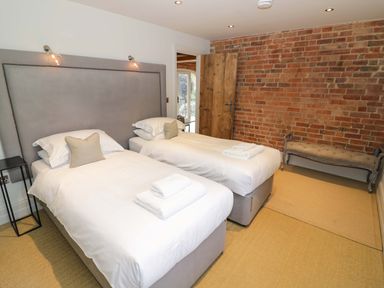 A bedroom with two single beds a wooden door and a bench against a brick wall at The Millhouse in Ledbury near Welland