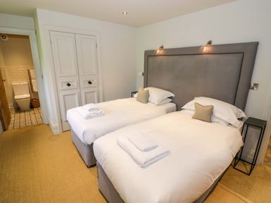 A bedroom with two single beds a large headboard and an open door showing a bathroom at The Millhouse in Ledbury near Welland