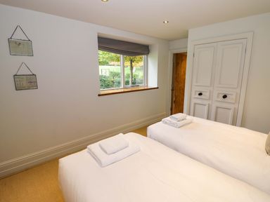A bedroom with two single beds with towels on them a window and a closed closet door at The Millhouse in Ledbury near Welland