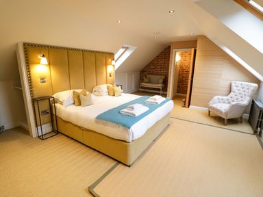 A bedroom with a large bed with a yellow headboard two bedside tables an armchair skylight and an open door at The Millhouse Ledbury near Welland