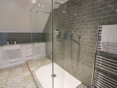 A bathroom with a walk in shower green tiled wall patterned floor a sink and a towel rack at The Millhouse in Ledbury near Welland
