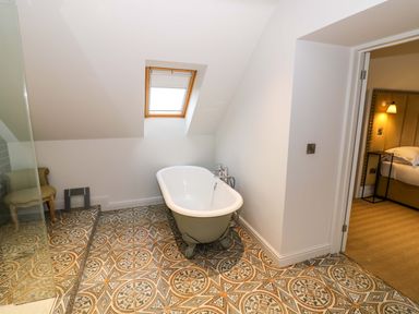 A bathroom with a freestanding bathtub under a skylight next to a doorway leading to a bedroom at The Millhouse in Ledbury near Welland