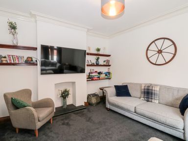 A living room with a gray sofa and armchair a wall-mounted tv and shelves with books and decorations at Castle Manor in Scarborough