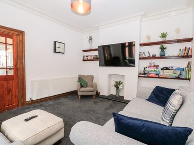 A living room with a wall-mounted television a gray sofa and armchair shelves with books and board games at Castle Manor in Scarborough