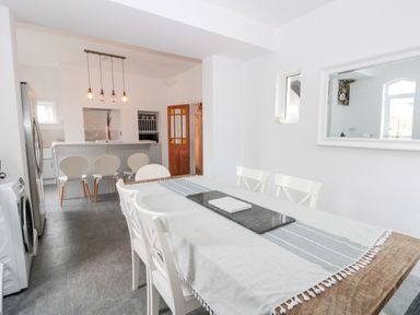 A dining area with a wooden table and white chairs next to a kitchen with a breakfast bar and stools at Castle Manor in Scarborough