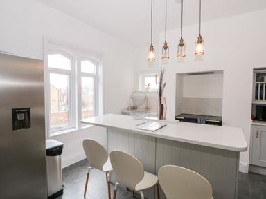 A kitchen with three white chairs at a white island and stainless steel refrigerator at Castle Manor in Scarborough