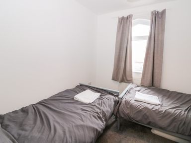 A bedroom with two single beds with gray bedding and white towels near a window with gray curtains at Castle Manor in Scarborough