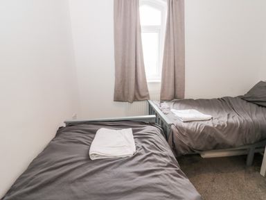 A bedroom with two single beds with dark gray bedding and white towels under a window with beige curtains at Castle Manor in Scarborough