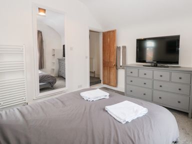 A bedroom with a gray bedspread and towels on the bed a gray dresser with a TV on top a wooden door and a large wall mirror at Castle Manor in Scarborough