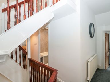 A hallway with wooden staircase railing a wall clock a radiator and doors leading to other rooms at Castle Manor in Scarborough