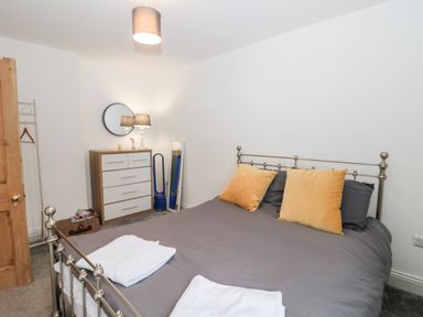 A bedroom with a metal bed frame gray bedding yellow pillows a dresser with a round mirror a standing mirror and a lamp at Castle Manor in Scarborough