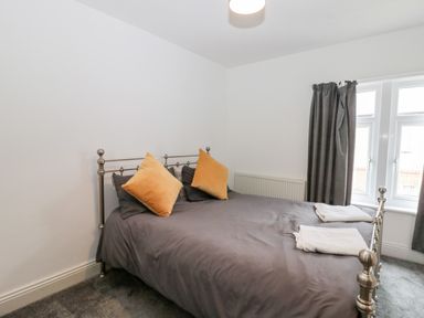 A bedroom with a metal bed frame grey bedding orange pillows folded towels on the bed and grey curtains at Castle Manor in Scarborough