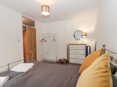A bedroom with a bed with gray bedding and yellow pillows a wooden door a white clothes rack a chest of drawers with a round mirror and a lamp at Castle Manor in Scarborough