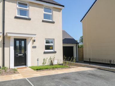 Front view of a beige house with black door and windows next to a garage and driveway at Pebble Bay in Appledore