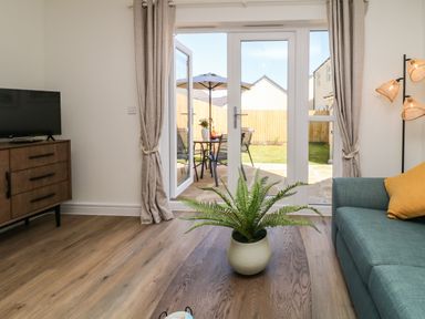 A living room with a green sofa a wooden cabinet a TV and glass doors opening to a garden at Pebble Bay in Appledore