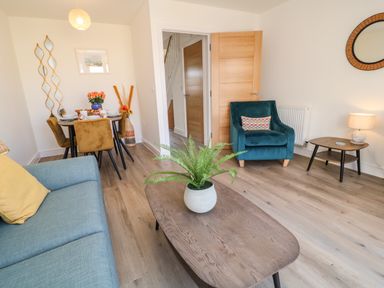 A living room with a blue couch a teal armchair a wooden coffee table with a plant and a dining table with four chairs at Pebble Bay in Appledore