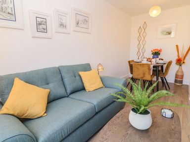 A blue sofa with yellow cushions a wooden table with a potted plant and a dining table with brown chairs in a living room at Pebble Bay in Appledore