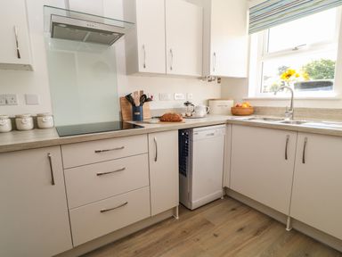 A kitchen with beige cabinets a countertop with bread a fruit basket a sink a window and a dishwasher at Pebble Bay in Appledore