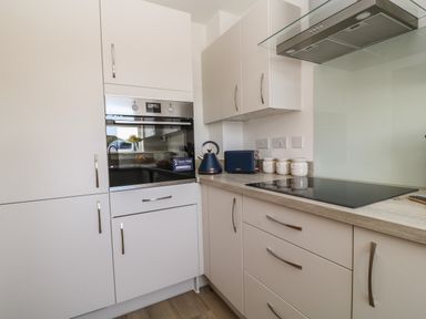 A kitchen with white cabinets a built-in oven a black electric cooktop and small appliances on the countertop at Pebble Bay in Appledore