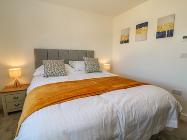 A bedroom with a double bed with pillows lamps on bedside tables and paintings on the wall at Pebble Bay in Appledore