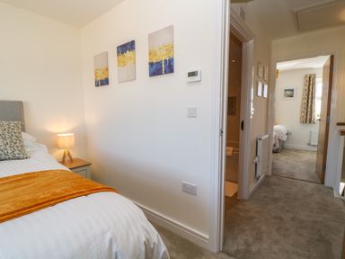 A bedroom with a bed lamp and artwork on the wall looking towards a hallway with an open door to another bedroom at Pebble Bay in Appledore