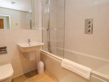 A bathroom with a sink a bathtub with a towel and a glass shower screen at Pebble Bay in Appledore