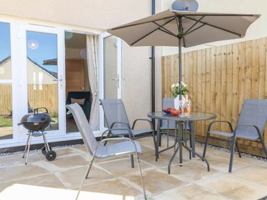 A patio with a round table, four chairs, an umbrella, and a barbecue grill at Pebble Bay in Appledore